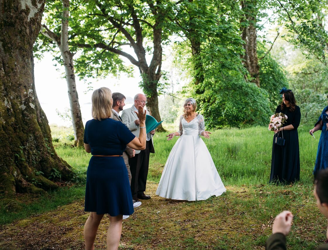 A deaf bride communicates with a Lipspeaker during an outdoor wedding ceremony, surrounded by guests and bridesmaids, celebrating connection and deaf identity.