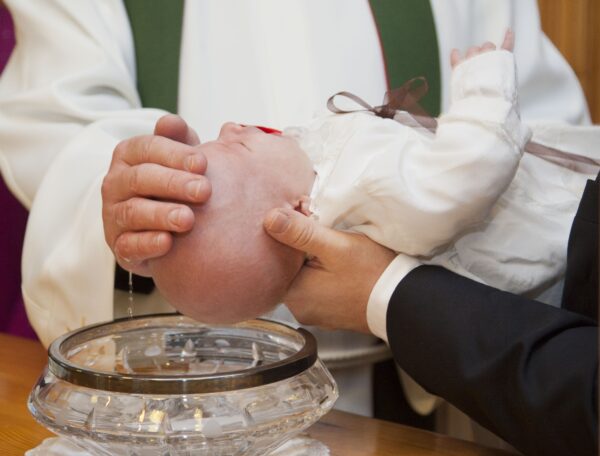 A baby being baptised, held by someone wearing a suit.