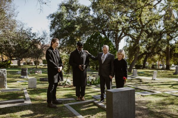A group of people gathered around a grave at a funeral. They are all wearing black.