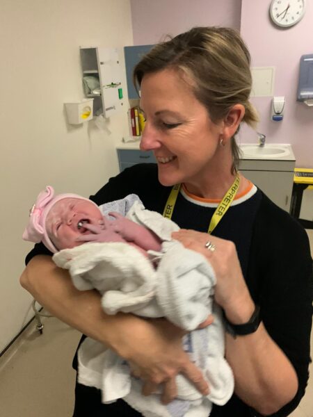 A BSL interpreter holding a newborn baby. The interpreter is smiling and the baby is yawning.
