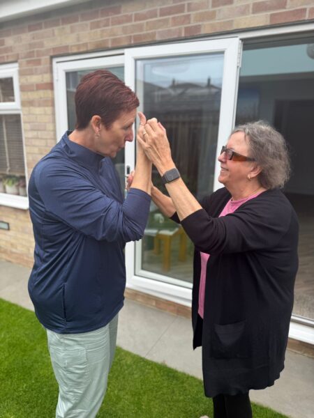 a deafblind connunicator is using hands on signing with a deafblind woman. They are standing in the garden outside the backdoor.