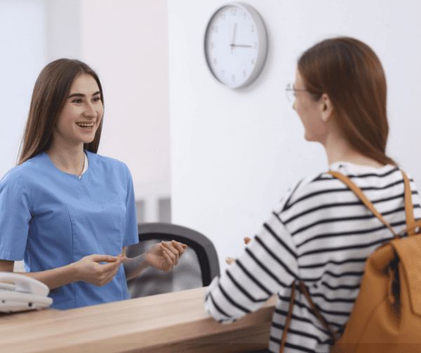 Healthcare professional speaking face-to-face with a patient at a reception desk, illustrating accessible communication in healthcare.